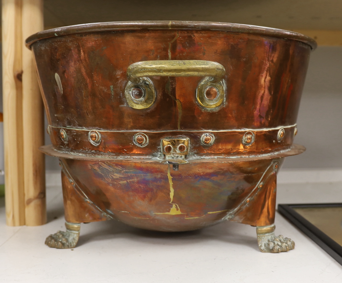 A large copper and brass two handled pail, raised on lion paw supports, 60cm wide including handles